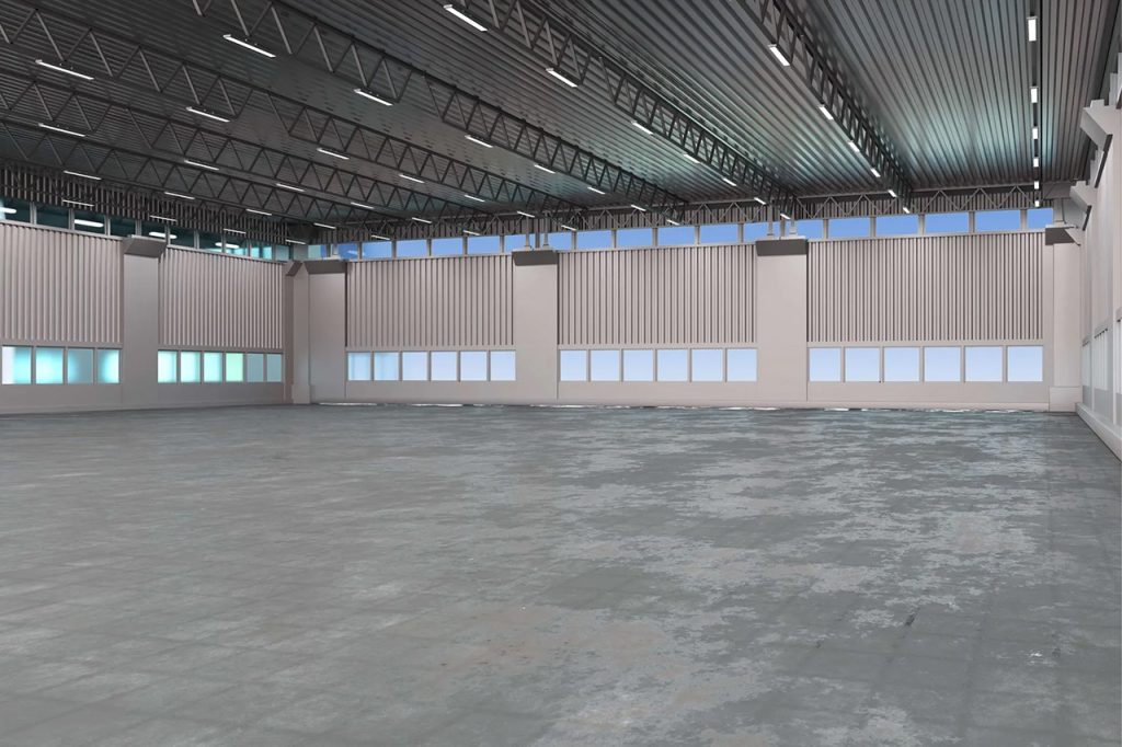 Spacious empty industrial warehouse with high ceilings, large windows, and exposed beams. The concrete floor is slightly worn, and natural light enters through the upper row of windows along the walls.