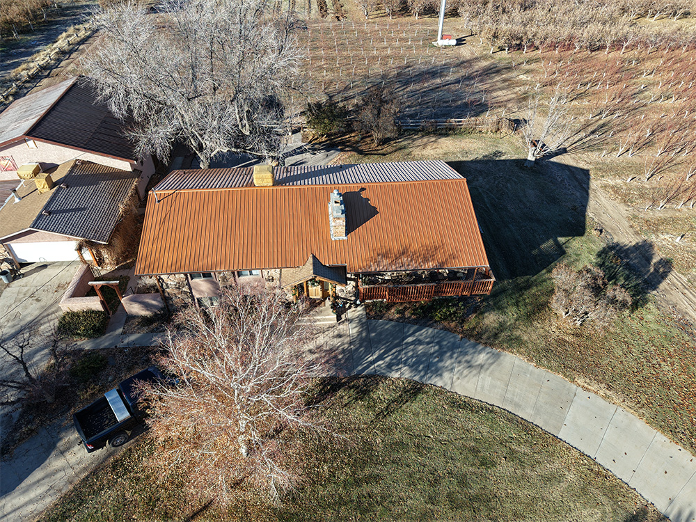 Aerial view of a house with a reddish-brown roof, surrounded by leafless trees and vineyards. A curved driveway leads to the house, with a black pickup truck parked nearby.